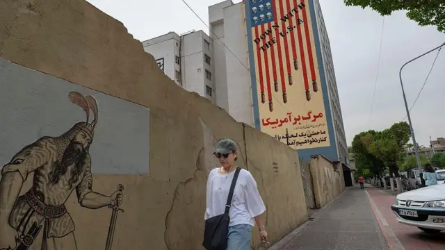 Una joven iraní camina por una acera bajo un mural antiestadounidense en el centro de Teherán, Irán.