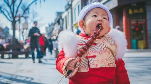 Un niño pequeño vestido de rojo comiendo dulces acaramelados.