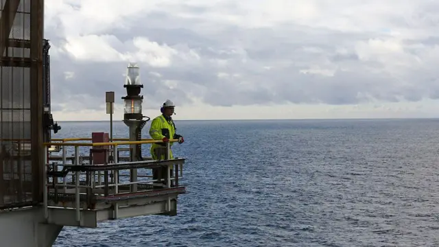 Un hombre observa la lejanía en un saliente de una plataforma en el mar.