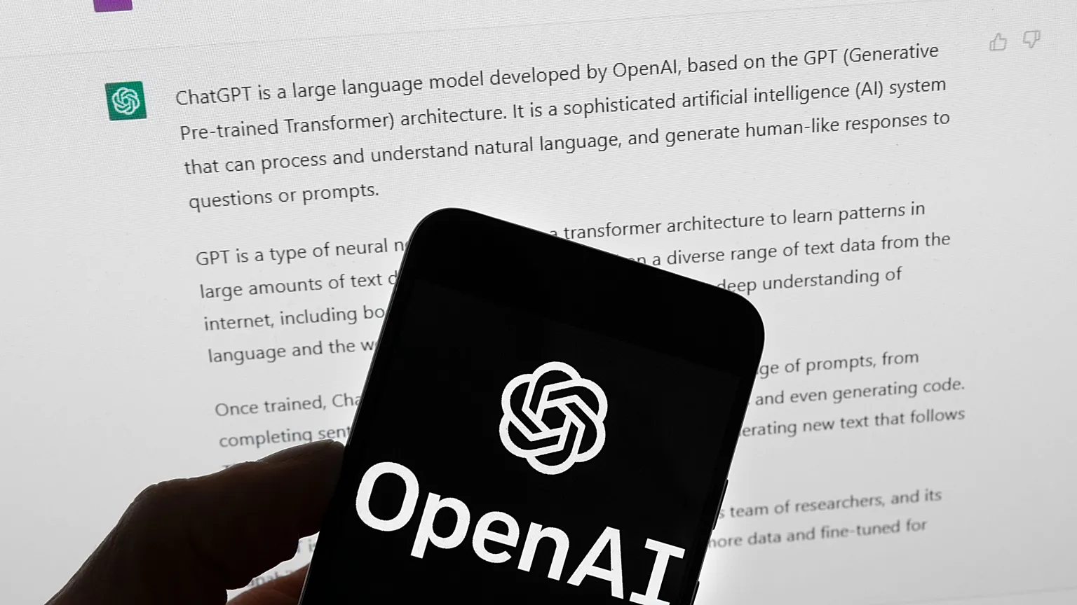 The OpenAI logo is seen on a mobile phone in front of a computer screen which displays output from ChatGPT, March 21, 2023, in Boston. 
