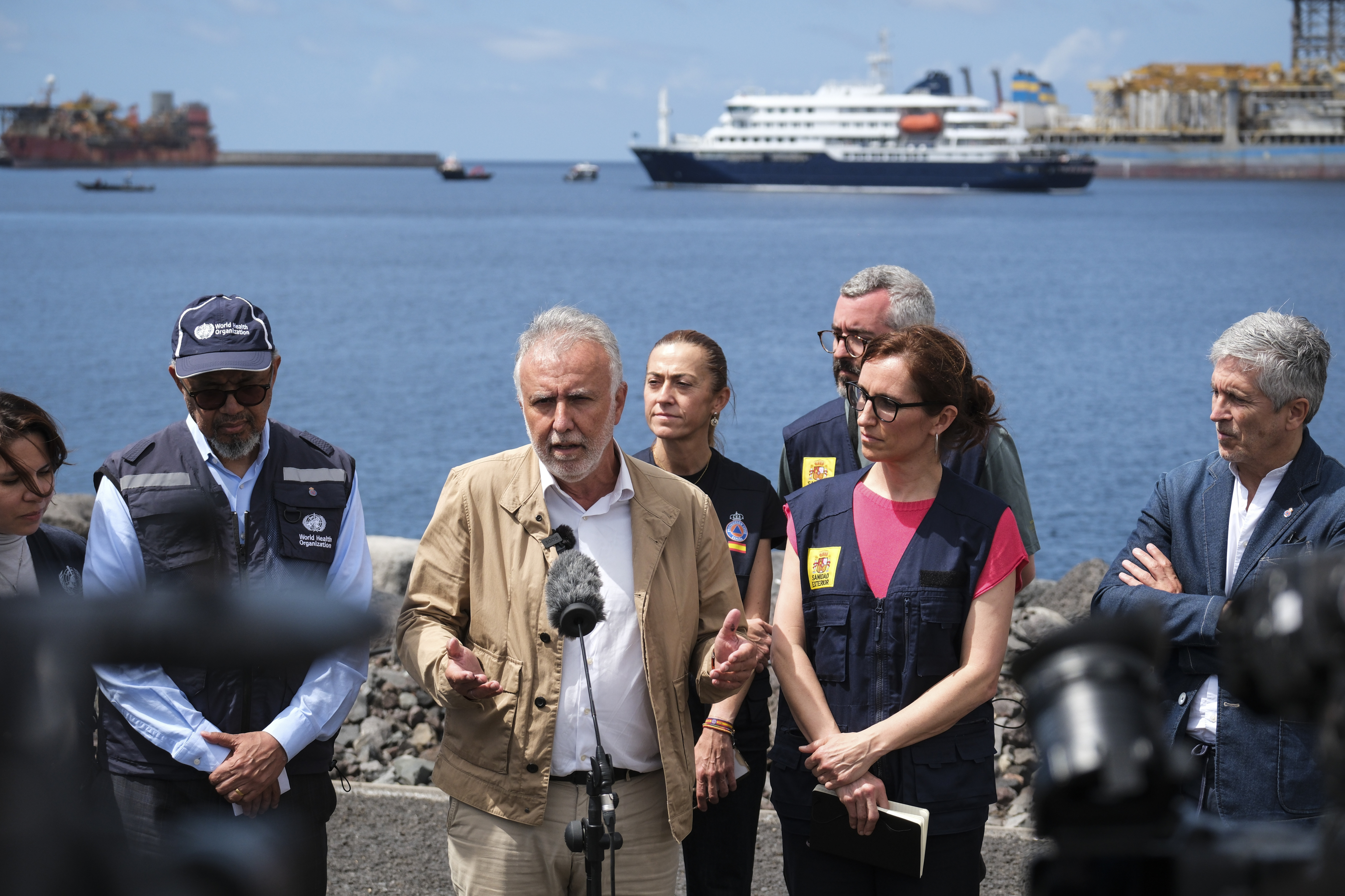 De izquierda a derecha, el director general de la OMS, Tedros Adhanom, y los ministros Ángel víctor Torres, Mónica García y Grande-Marlaska en el puerto de Granadilla. Tras ellos, el MV Hondius fondeado.