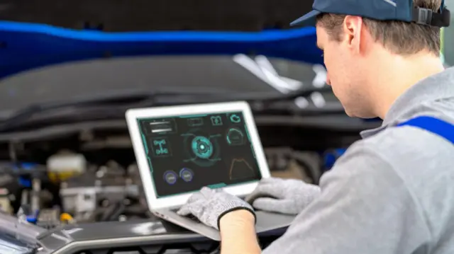 Un hombre registrando una computadora sobre un auto. 