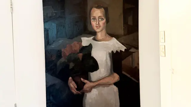 Un cuadro que se cree que es el "Retrato de una joven" de Toon Kelder muestra a una niña con un vestido blanco de mangas negras que sostiene lo que parece ser un ramo de flores rojas. Tiene el pelo castaño y los ojos azules, y está sentada.