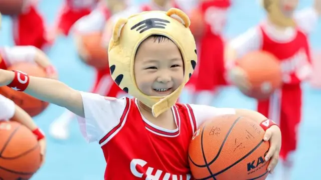 Un niño pequeño sonriendo sostiene una pelota de básquetbol.