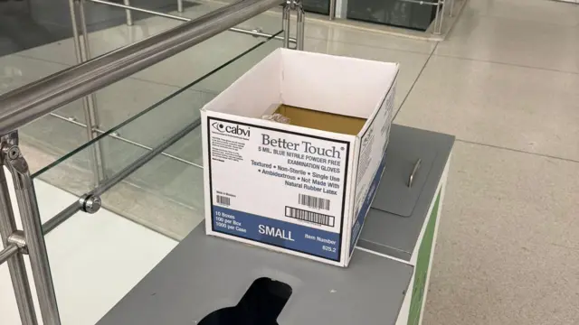 Una caja de cartón blanca con texto azul yace sobre una mesa en un aeropuerto. 