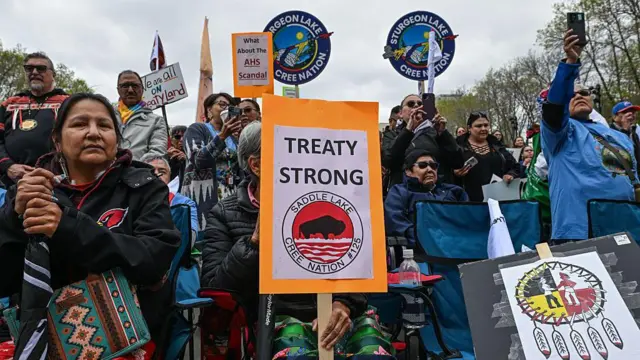 Una imagen que muestra a decenas de miembros de las Primeras Naciones reunidos frente a la legislatura de Alberta en Edmonton, sosteniendo carteles que dicen FIRME CON EL TRATADO y TODOS VIVIMOS EN TIERRA BAJO TRATADO