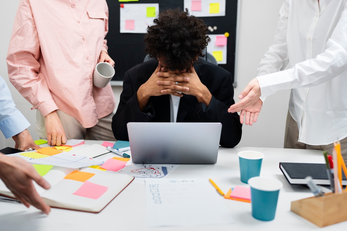 Un empleado estresado en su puesto de trabajo, mientras sus compañeros lo rodean. (Freepik)