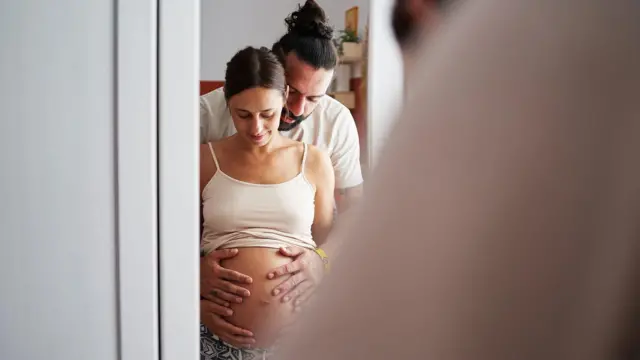 Una pareja embarazada se mira al espejo.