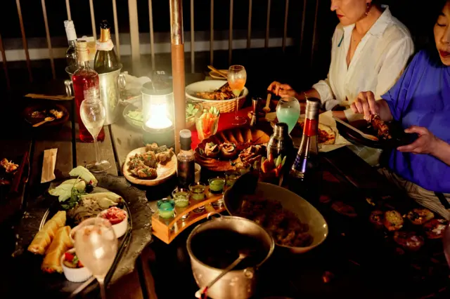 Una mesa con distintos platos en la noche y un grupo de amigos que se reunió a cenar.
