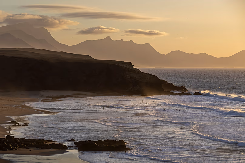 People wade in the Atlantic Ocean during sunset at the La Pared beach on the Canary Island of Fuerteventura, 6 October, 2025