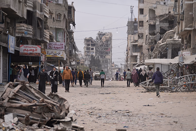 Palestinians walk along a street surrounded by buildings destroyed during the Israel Hamas war in Gaza City, 15 May, 2026