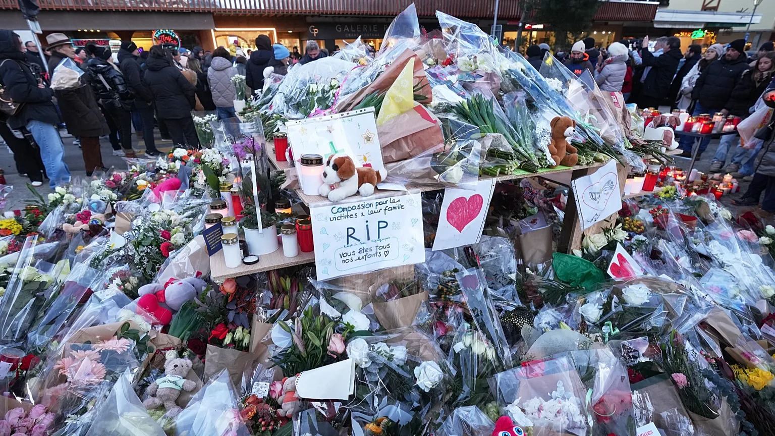  People stand around floral tributes and candles placed outside the sealed off Le Constellation bar in Crans-Montana, Switzerland, on Jan. 3, 2026 (AP Photo/ Antonio Calanni)