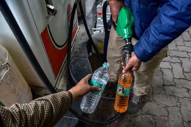 Unos hombres llenan unas botellas con gasolina en una estación de servicio.