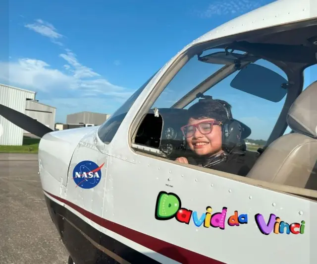 David en la cabina de una avioneta donde está impreso el nombre "David da Vinci" y un logo de la NASA.