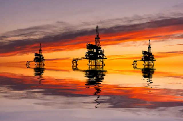 Tres plataformas petroleras en el mar durante el atardecer.