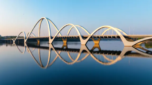 Una foto de un puente moderno con varios bordes curvos que se reflejan en el agua.