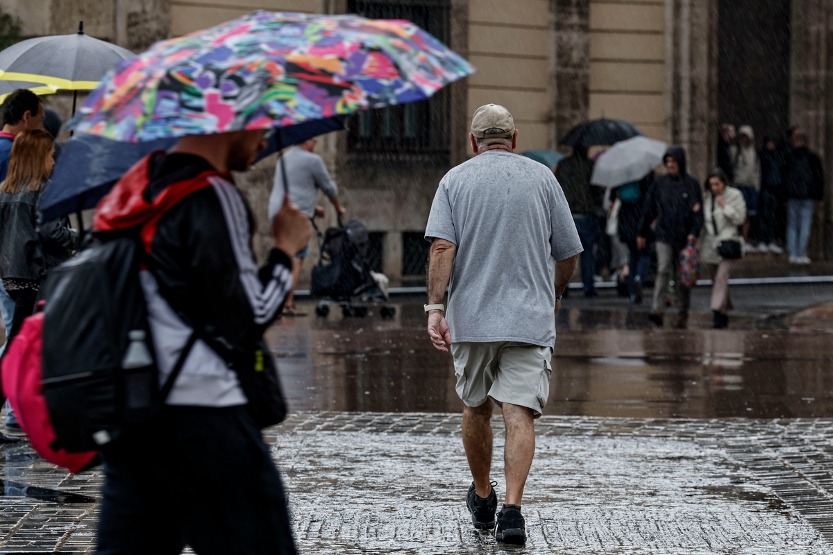 Numerosas personas se protegen de la lluvia con paraguas mientras pasean por la plaza del Ayuntamiento de Valencia, a 1 de mayo de 2026. (EFE/Manuel Bruque)