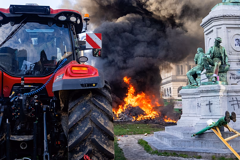 Manifestantes queman basura cerca de una estatua y un tractor durante una protesta de agricultores europeos frente al Parlamento Europeo en Bruselas, jueves 18 de diciembre de 2025.