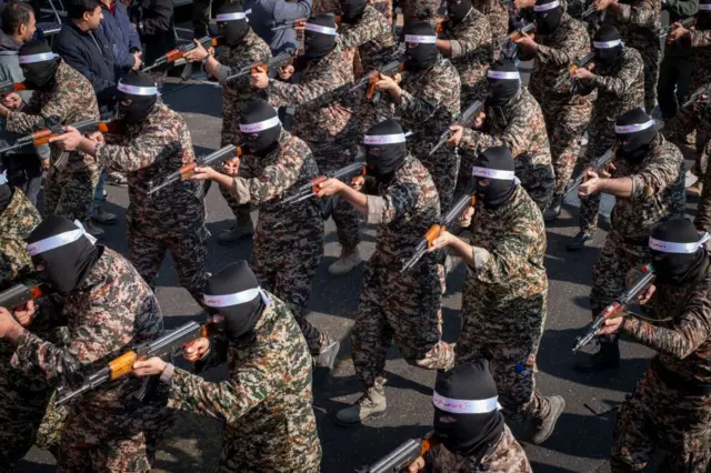 Varios miembros del CGRI, vestidos con indumentaria militar y pasamontañas negros, apuntan con sus armas durante un ejercicio.