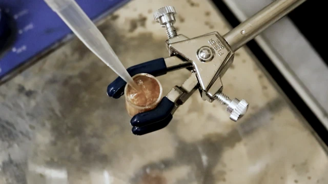 Una pipeta está sostenida cerca de un tubo de ensayo que contiene un gel marrón. Forma parte de un experimento de almacenamiento molecular de energía solar térmica en la Universidad de California, Santa Bárbara