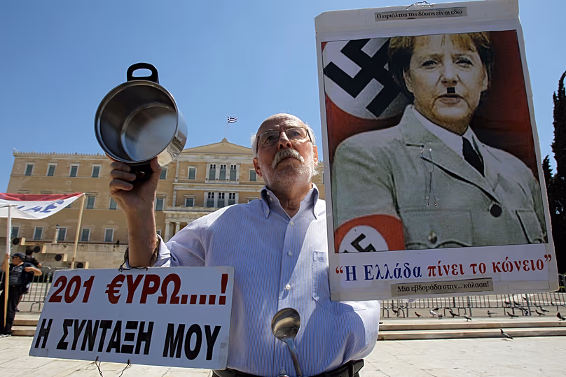 An elderly man holds a poster with a picture of German Chancellor Angela Merkel, made to look like Adolf Hitler during a protest in Athens. May 1, 2013 (AP Photo/Thanassis) 
