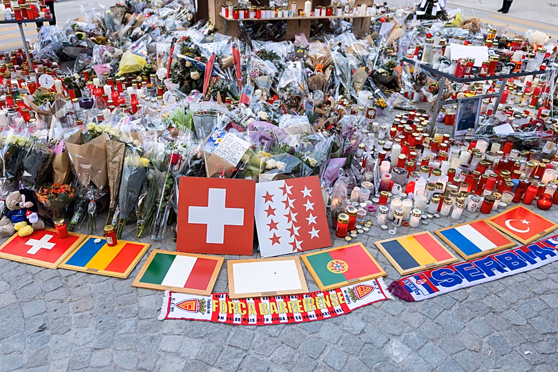Plaques bearing international flags are placed alongside flowers and candles at the "Le Constellation" bar in Crans-Montana, 6 January, 2026