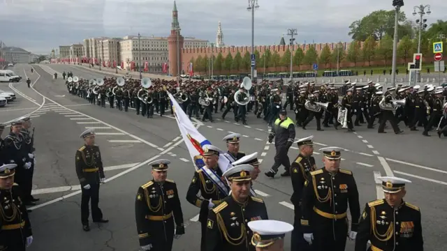 Militares rusos caminan en grupos por una calle vacía, algunos portando instrumentos de viento.