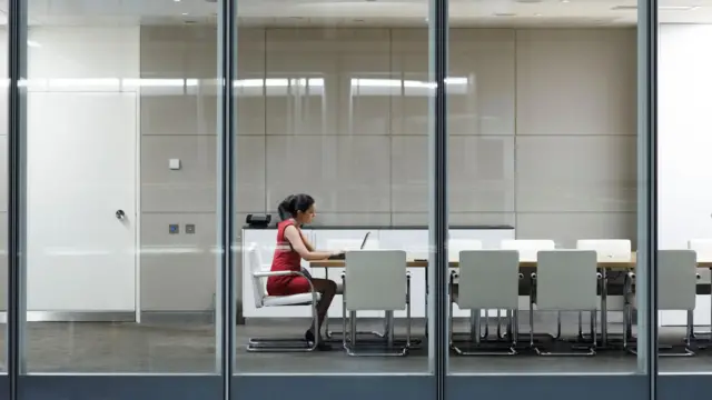 Una mujer con vestido rojo sentada en una oficina de sillas blancas con su laptop y trabajando