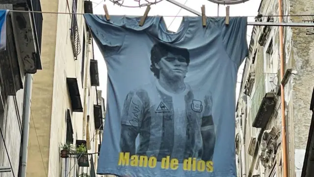 Una camiseta con el rostro de Maradona y la inscripción "Mano de dios" en las calles del centro histórico al día siguiente del primer aniversario de la muerte de Diego Armando Maradona el 26 de noviembre de 2021 en Nápoles (Italia). 