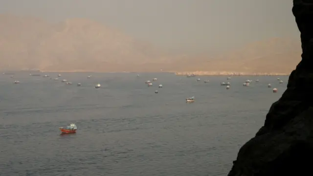 Se observa el estrecho de Ormuz a lo lejos, con varios buques cisterna y cargueros. En primer plano y en la distancia se aprecian montañas.