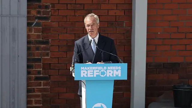 El líder de Reform UK, Nigel Farage, habla en una conferencia de prensa sobre un atriz azul claro.