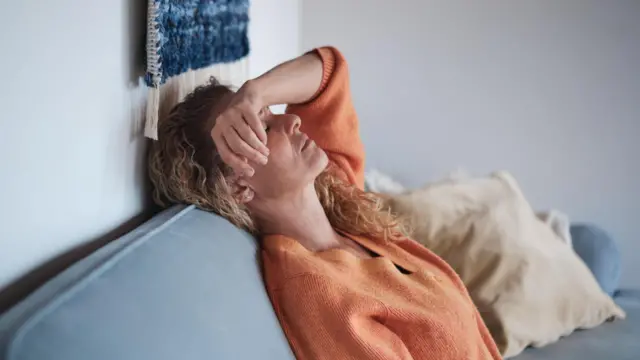 Una mujer tirada en un sillón con una mano en la cabeza.