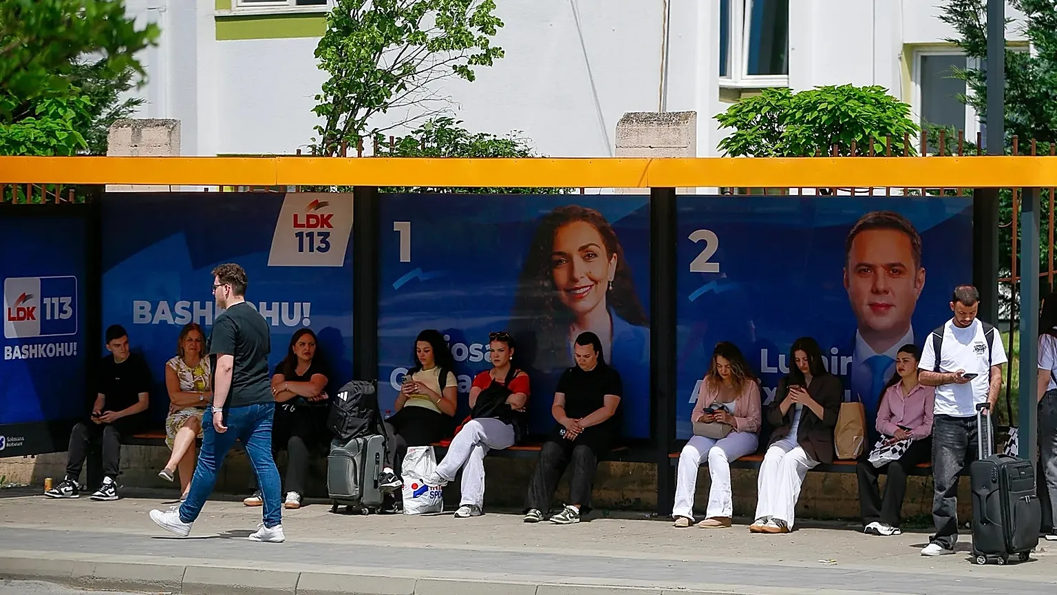 People wait at a bus station displaying election posters in capital Pristina, 5 June, 2026