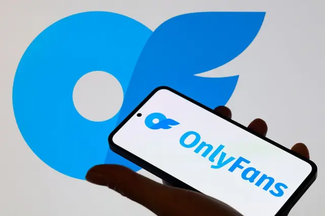 Una persona sostiene un móvil en la mano, el cual tiene el logo de OnlyFans en azul