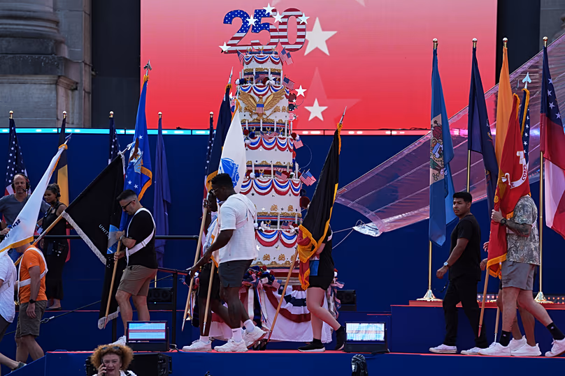 People carry flags past a giant birthday cake to celebrate during the America 250 event in Brussels, Sunday, June 28, 2026. (AP Photo/Virginia Mayo)