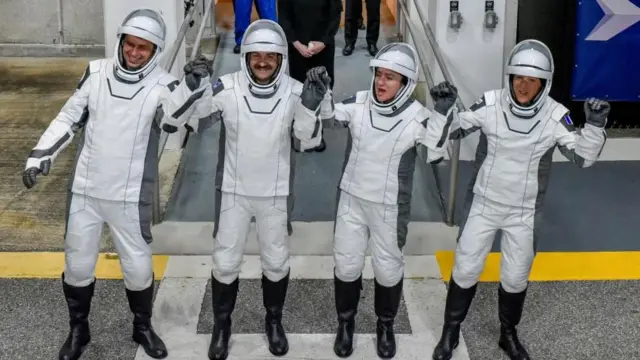 Cuatro astronautas con trajes espaciales blancos se toman de las manos y las alzan en señal de celebración a la entrada del Centro Espacial Kennedy.