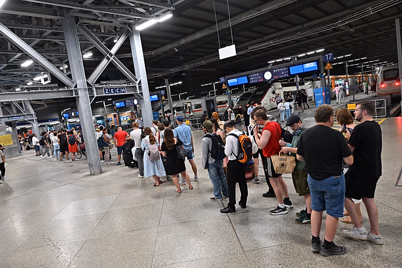Passengers stand in line at the DB information desk at the Munich train station, Tuesday, June 23, 2026