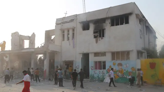 Imagen fija que muestra las consecuencias del ataque a Minab. El exterior del edificio está gravemente dañado y se ve a gente fuera inspeccionándolo. 