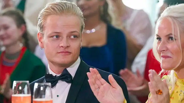 Marius Borg Høiby vestido de traje y con pajarita observa mientras su madre, la futura reina de los noruegos, con un vestido amarillo aplaude.
