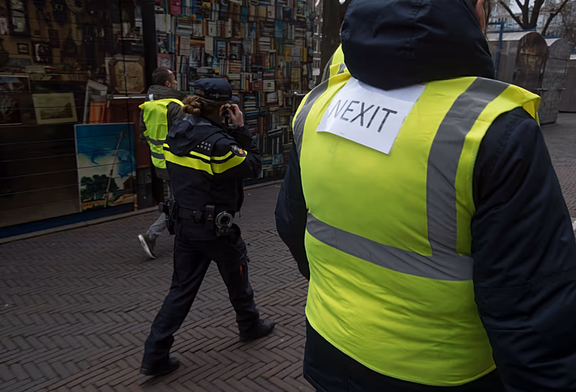 A demonstrator carries a NEXIT sign on his yellow vest as a Dutch Police officer walks alongside a peaceful demonstration in Amsterdam, Netherlands, Saturday, Dec. 8, 2018. 