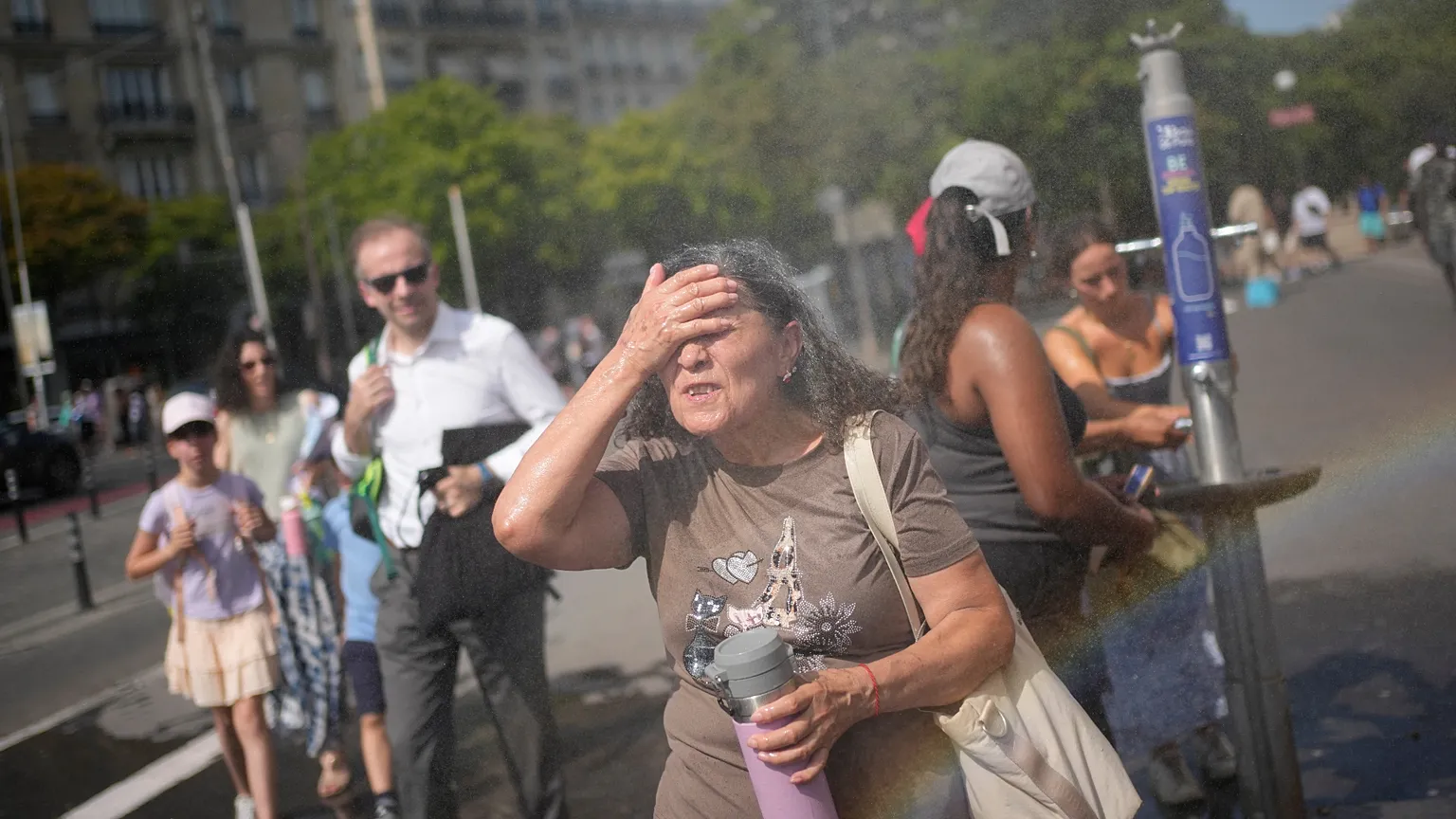 Tourists enjoy cooling off at a public water fountain In Paris, Friday, June 26, 2026. (AP Photo/Christophe Ena )