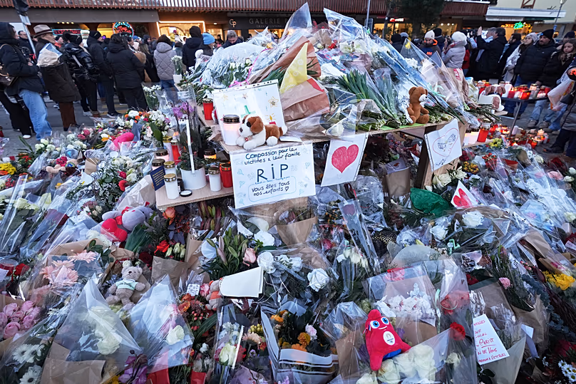 People stand around floral tributes and candles placed outside the sealed off Le Constellation bar in Crans-Montana, Swiss Alps, Switzerland, on Jan. 3, 2026.