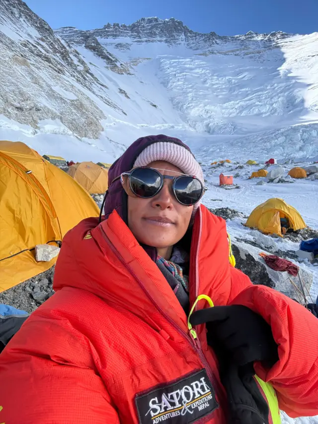 Purnima Shrestha se toma una selfie en un campamento en el Everest. Lleva gafas de sol, un sombrero rosa y un gran abrigo rojo.