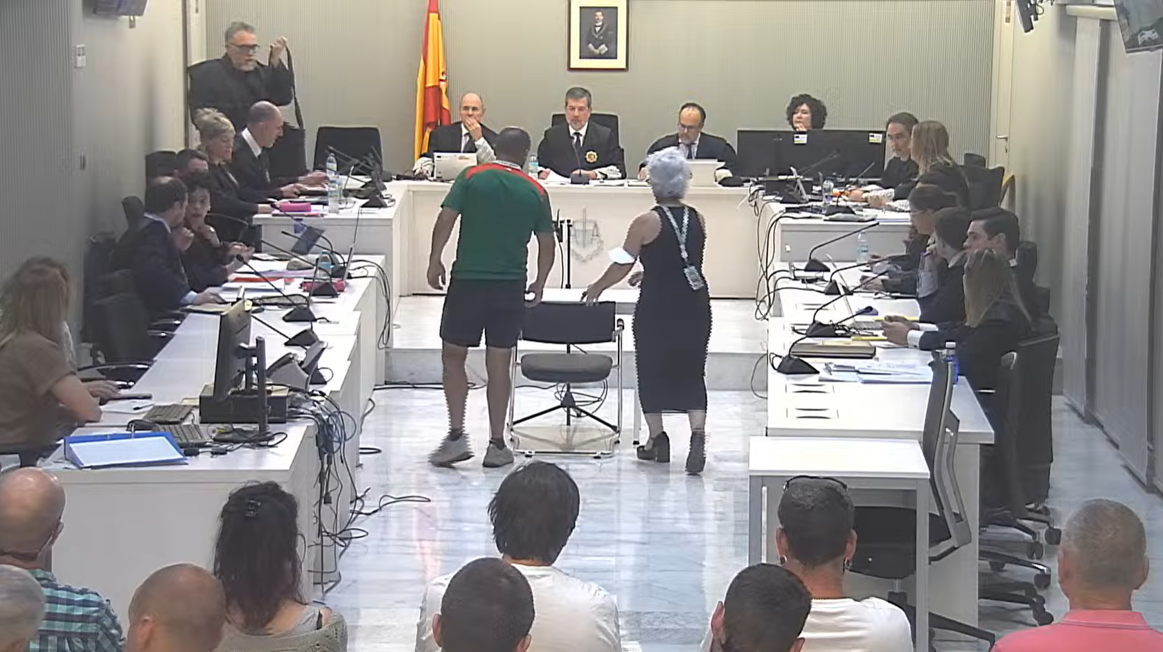 El letrado expulsado se prepara a abandonar el juicio mientras su cliente se sienta ante el tribunal.