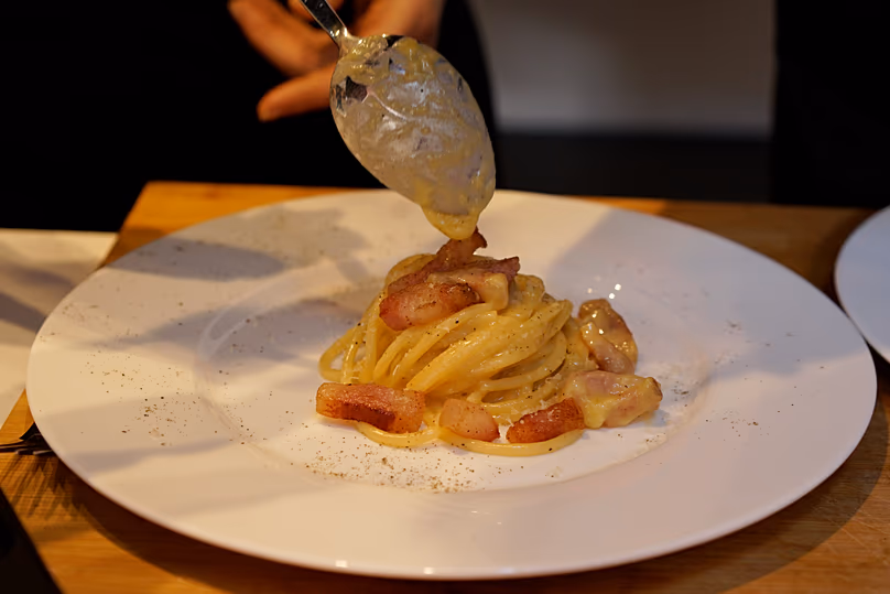 A creamy mix of grated pecorino cheese and egg drops from a spoon in Rome during Carbonara Day