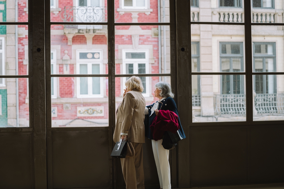 Dos mujeres mayores miran a través de una ventana (Canva)