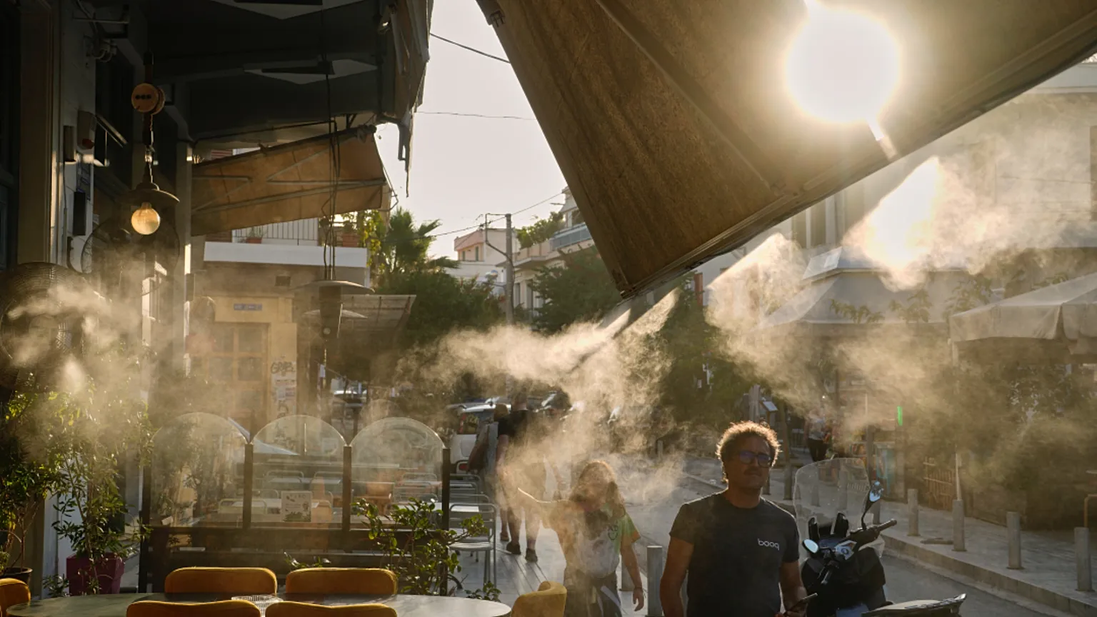 Pedestrians walk next to a mist machine in Thisio district of Athens during a heatwave, July 2025.