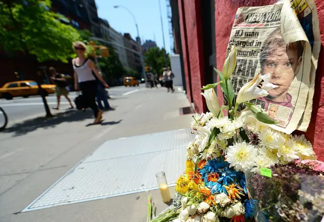 Un arrume de flores sobre el cual se apoya un periódico en el que se ve una foto de Etan