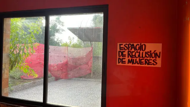 Otra imagen del interior del memorial. En ella se ve una gran ventana con un cartel junto a ella, colgado en una pared de color rojo vivo, en el que se lee "Espacio de reclusión de mujeres".