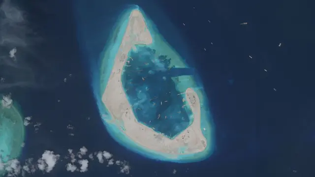 Las imágenes satelitales de Vantor muestran una vista general del Arrecife Antelope, incluyendo una laguna parcialmente cerrada, áreas de arena recuperada y numerosas embarcaciones operando en sus alrededores. La imagen proporciona un contexto más amplio de la expansión visible y la actividad marina que se observa en el arrecife.